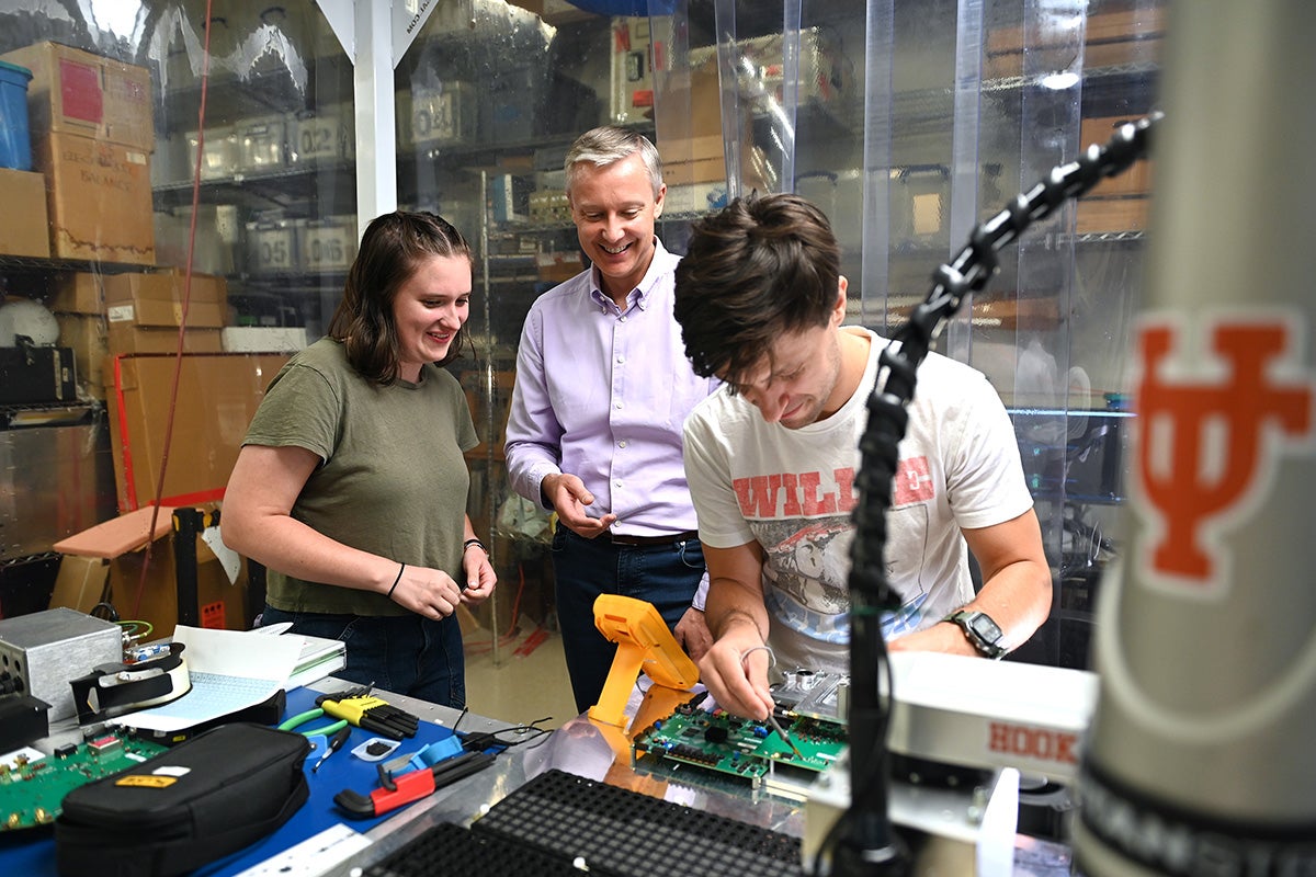 A scientist with two students working in a lab with electronics